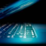 Close-up van een verlicht laptoptoetsenbord in blauw licht met halfgesloten scherm