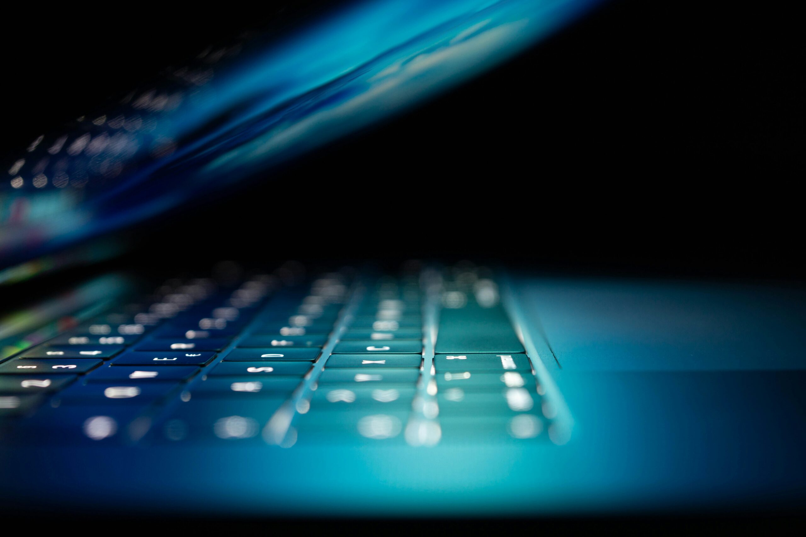 Close-up van een verlicht laptoptoetsenbord in blauw licht met halfgesloten scherm
