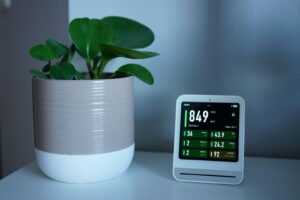 Slimme thermostaat op tafel naast een plant, met display dat energie- en luchtkwaliteitsgegevens toont.
